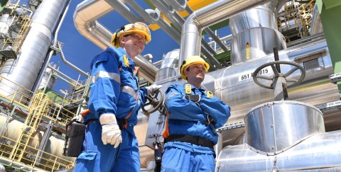 Zwei Arbeitnehmer in Arbeitskleidung in einer Raffinerie mit Rohren und Maschinen