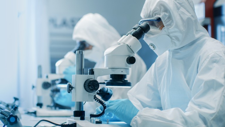 Zwei Wissenschaftler in Sterilreinigungsgeräten setzen Mikroskope für Forschung ein